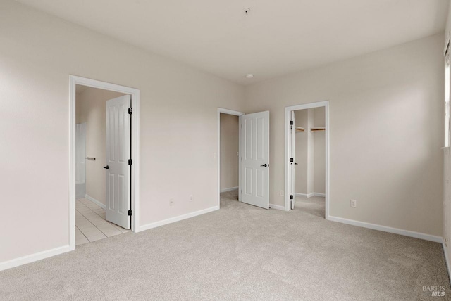 unfurnished bedroom with connected bathroom, light carpet, baseboards, light tile patterned floors, and a spacious closet