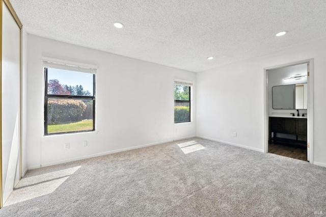 unfurnished bedroom featuring a textured ceiling, carpet, baseboards, ensuite bath, and recessed lighting