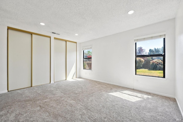 unfurnished bedroom with visible vents, two closets, a textured ceiling, carpet flooring, and multiple windows