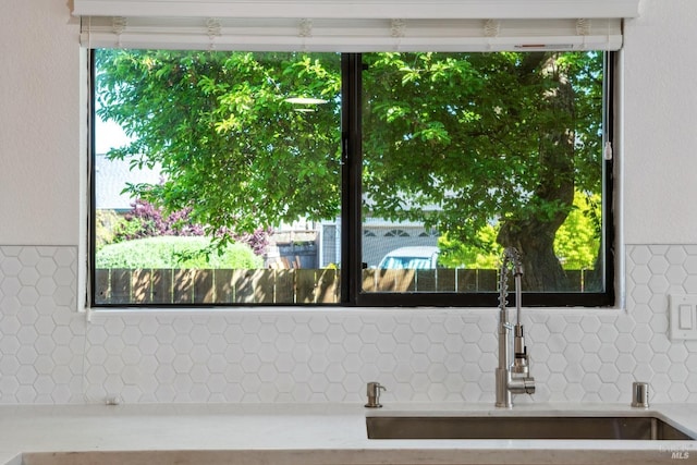 interior details featuring light countertops, tasteful backsplash, a textured wall, and a sink