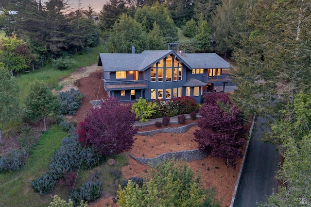 exterior space featuring a chimney, roof with shingles, a balcony, and a wooded view