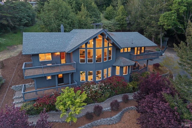 rear view of house featuring a wooded view, a shingled roof, and a balcony