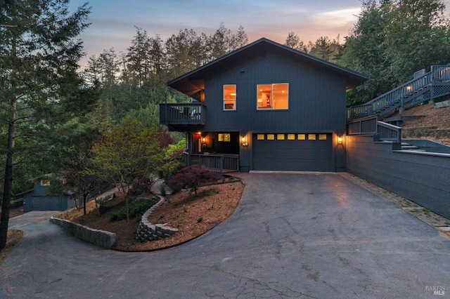 view of front of property featuring a garage, aphalt driveway, stairway, and a balcony