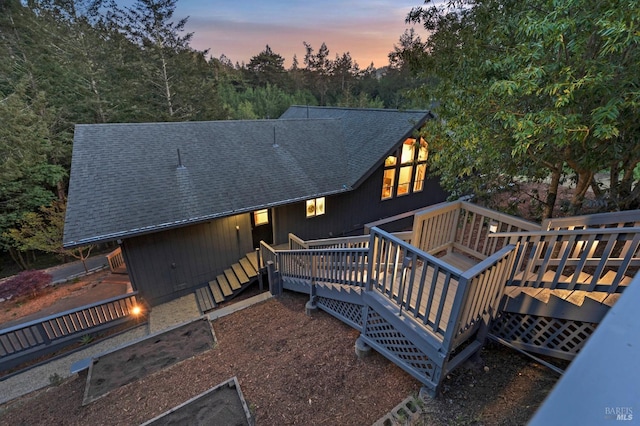 back of property at dusk with a deck and roof with shingles