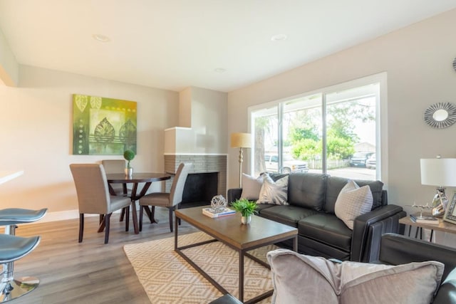 living area with baseboards, a brick fireplace, and wood finished floors