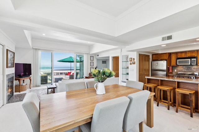 dining area with a raised ceiling, visible vents, a high end fireplace, recessed lighting, and light carpet