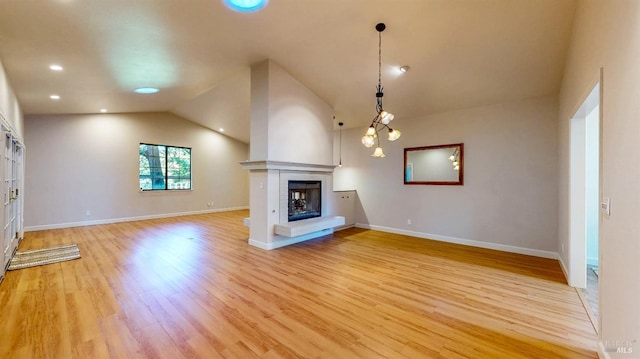 unfurnished living room with vaulted ceiling, baseboards, a fireplace with raised hearth, and light wood-style floors