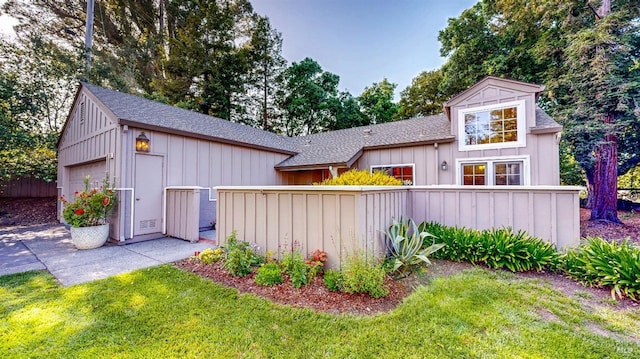 back of house featuring a yard, roof with shingles, fence, and board and batten siding