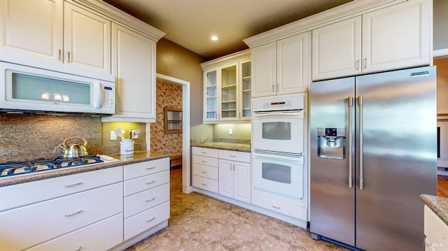 kitchen featuring stone countertops, white appliances, glass insert cabinets, and tasteful backsplash