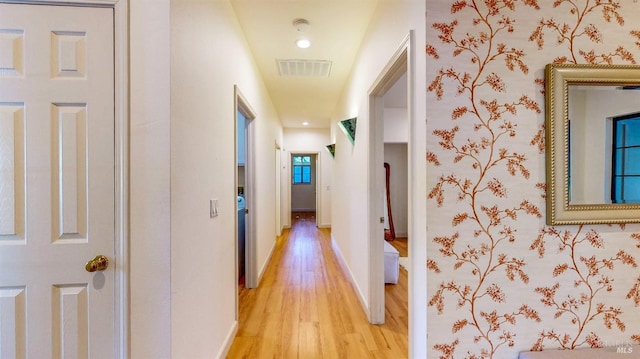 hallway with light wood-style floors, visible vents, and baseboards