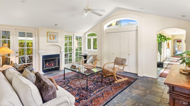 living room with a fireplace with flush hearth, vaulted ceiling, arched walkways, stone tile flooring, and ceiling fan