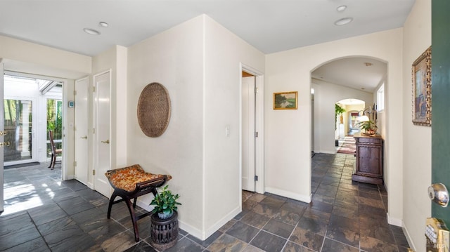 hall with stone tile floors, baseboards, arched walkways, and recessed lighting