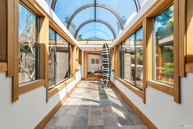 unfurnished sunroom featuring stone tile flooring and baseboards