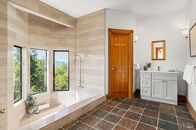 bathroom with a tile shower, baseboards, stone tile floors, and vanity