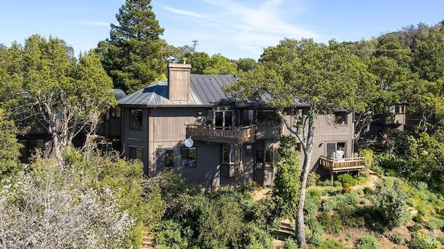 rear view of property featuring a chimney, a standing seam roof, a balcony, and metal roof