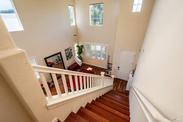 stairway featuring baseboards, wood finished floors, a high ceiling, and a wealth of natural light