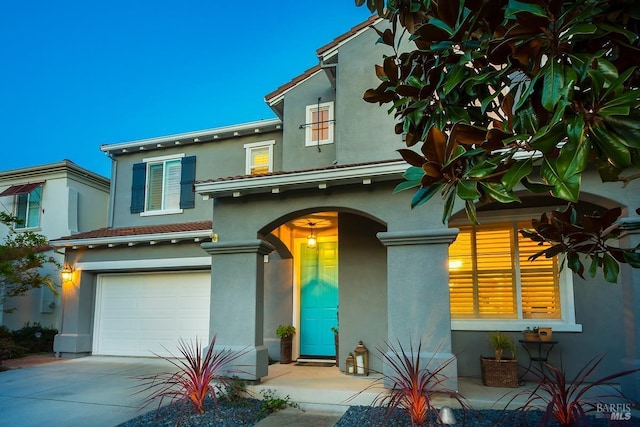 mediterranean / spanish-style home with stucco siding, an attached garage, and a tiled roof