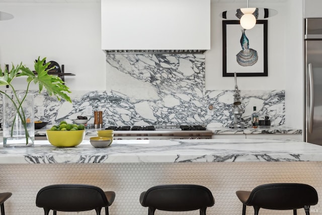 kitchen featuring decorative backsplash, stainless steel refrigerator, a breakfast bar area, and light stone counters