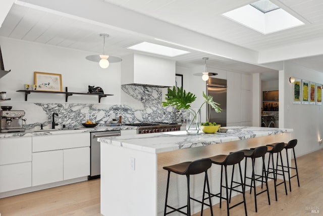 kitchen featuring stainless steel appliances, open shelves, a sink, a skylight, and decorative backsplash