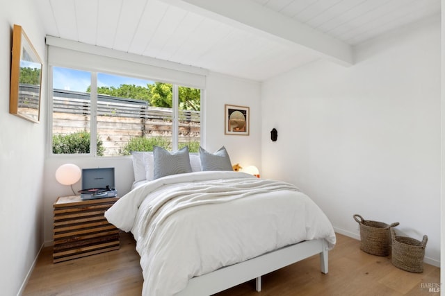 bedroom featuring baseboards, wood finished floors, and beam ceiling