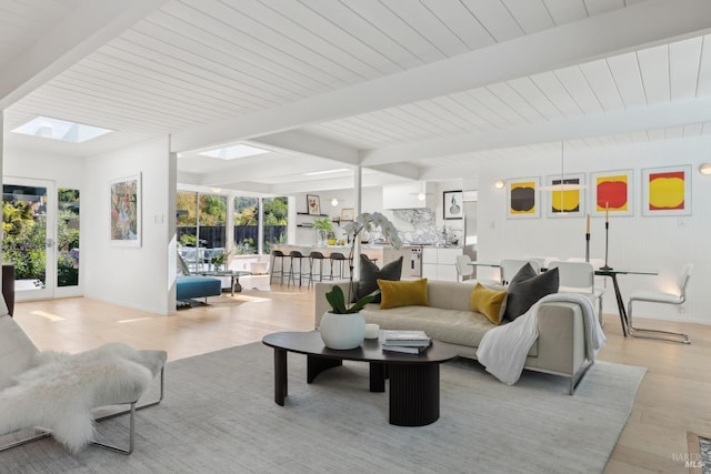 living area featuring light wood finished floors, a skylight, baseboards, and beamed ceiling