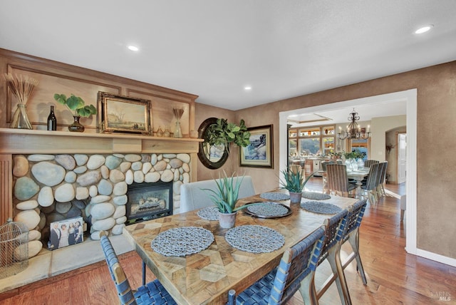 dining area with baseboards, wood finished floors, a fireplace, and an inviting chandelier
