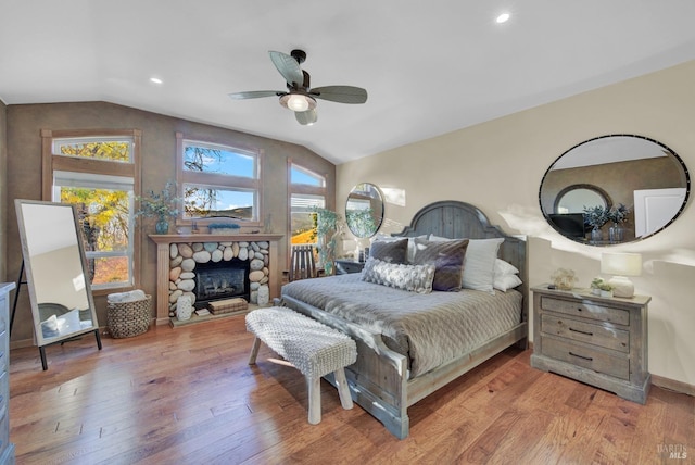 bedroom with vaulted ceiling, a ceiling fan, a stone fireplace, hardwood / wood-style flooring, and recessed lighting