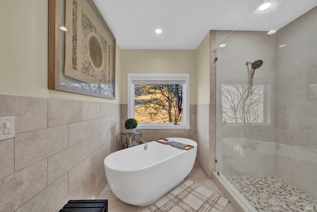 bathroom featuring wainscoting, tile walls, walk in shower, a soaking tub, and tile patterned flooring