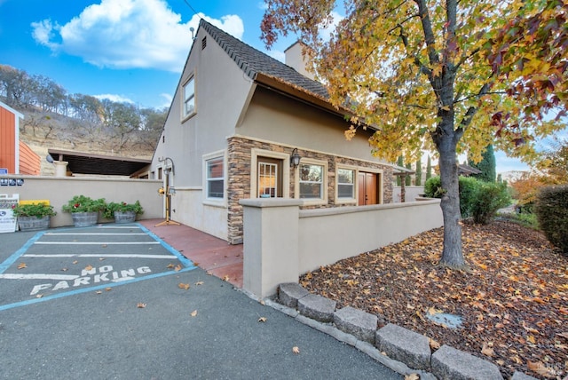 view of front of property with stucco siding, a chimney, stone siding, and fence private yard