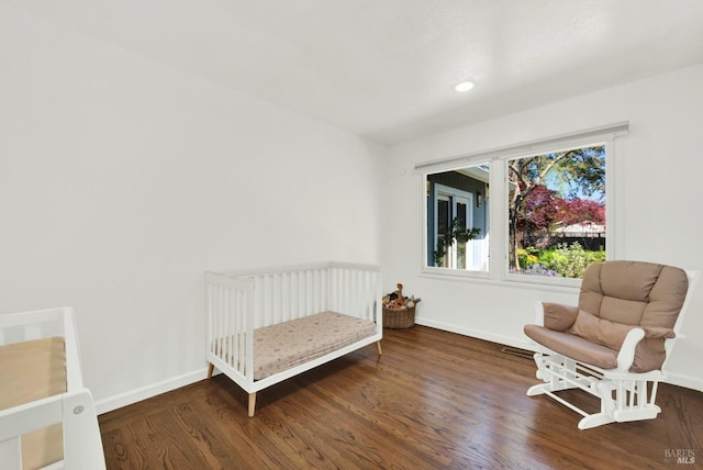 bedroom featuring a nursery area, baseboards, and wood finished floors