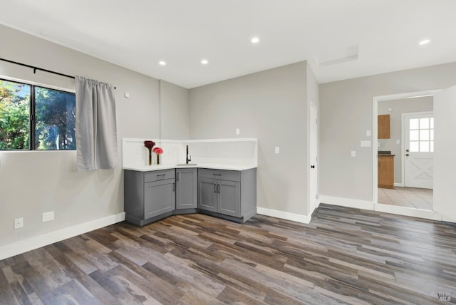 kitchen with baseboards, gray cabinetry, a sink, and dark wood finished floors