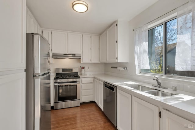 kitchen featuring a sink, light countertops, under cabinet range hood, stainless steel appliances, and white cabinetry