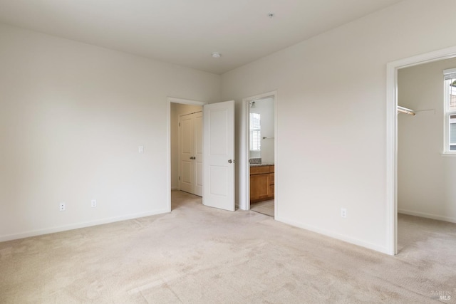 unfurnished bedroom featuring light carpet, baseboards, a closet, ensuite bath, and a walk in closet