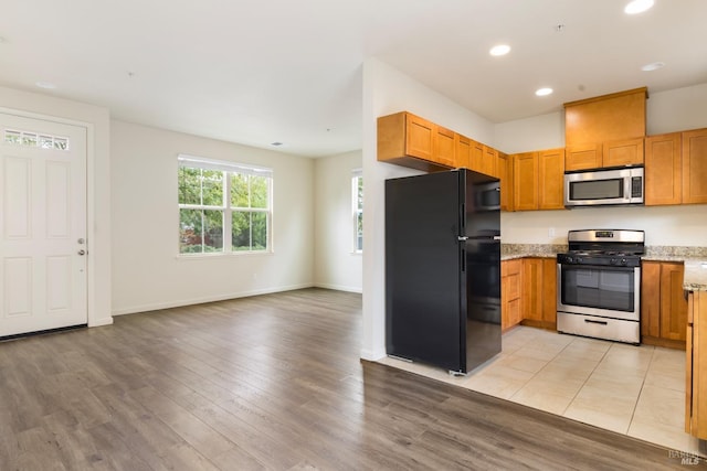 kitchen featuring recessed lighting, light stone counters, stainless steel appliances, light wood-style floors, and open floor plan