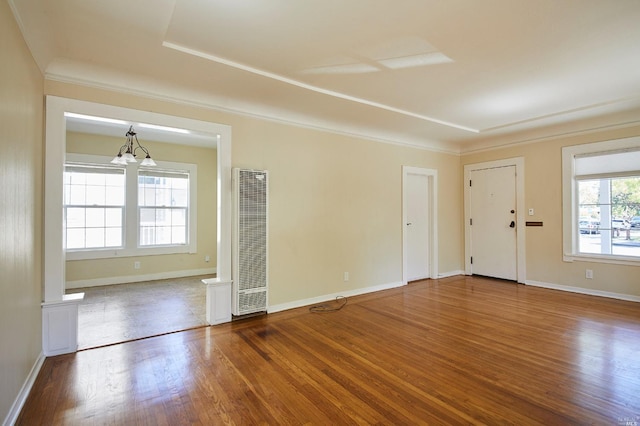 spare room with a chandelier, wood finished floors, baseboards, and a heating unit