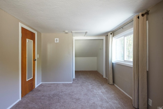 unfurnished bedroom with light carpet, a closet, baseboards, attic access, and a textured ceiling