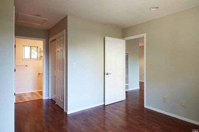 unfurnished bedroom with wood finished floors, a closet, attic access, baseboards, and a heating unit