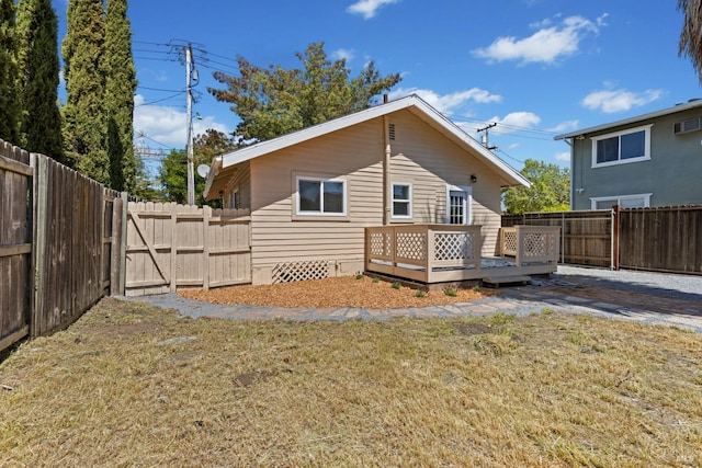 rear view of property featuring a fenced backyard, a gate, a deck, and a lawn