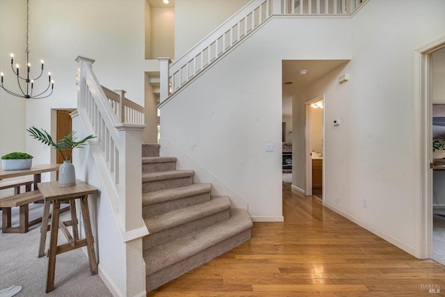 stairway featuring a chandelier, baseboards, wood finished floors, and a towering ceiling