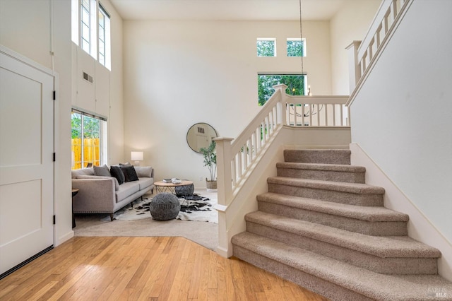 stairway featuring baseboards, a towering ceiling, visible vents, and hardwood / wood-style floors