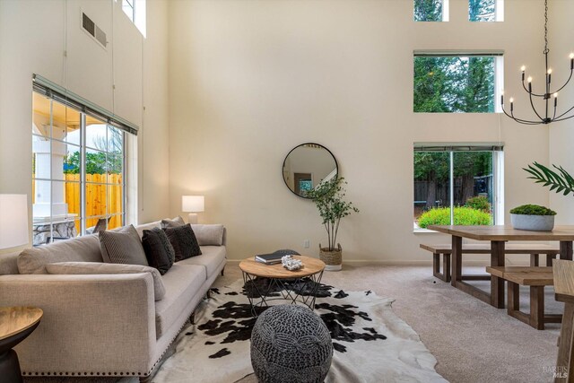 carpeted living area with plenty of natural light, visible vents, a towering ceiling, and an inviting chandelier