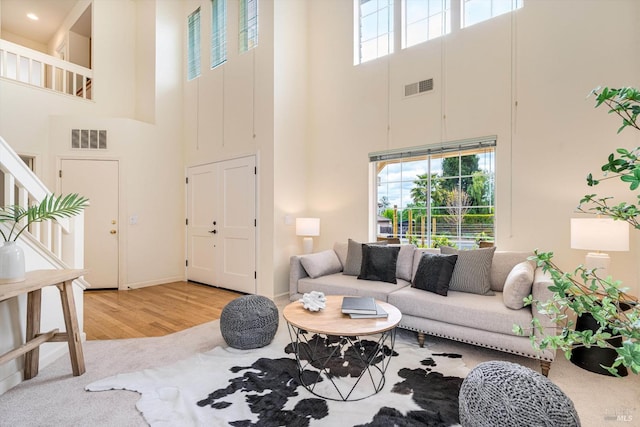 living room with wood finished floors, visible vents, a towering ceiling, and baseboards