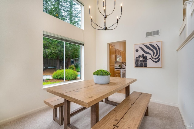 dining area featuring a notable chandelier, visible vents, light carpet, and a high ceiling