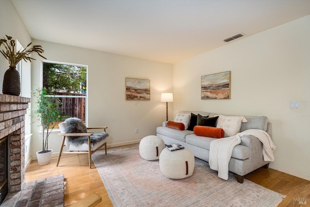 living room featuring baseboards, a brick fireplace, light wood-style floors, and visible vents