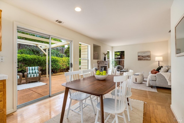 dining space featuring recessed lighting, a brick fireplace, light wood-style flooring, and visible vents