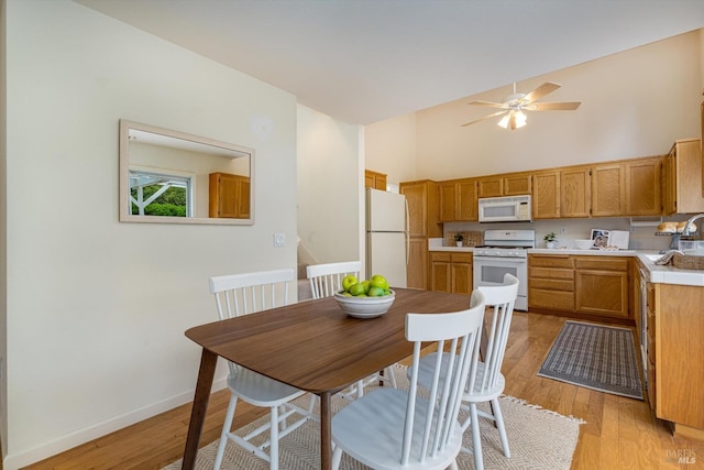 kitchen featuring high vaulted ceiling, white appliances, light wood-type flooring, ceiling fan, and light countertops