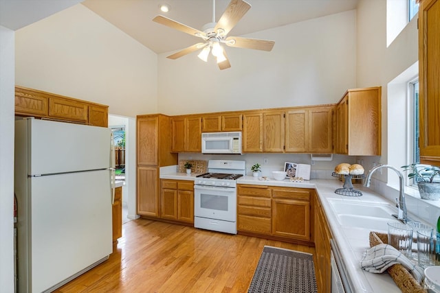 kitchen featuring high vaulted ceiling, a ceiling fan, a sink, white appliances, and light wood-type flooring