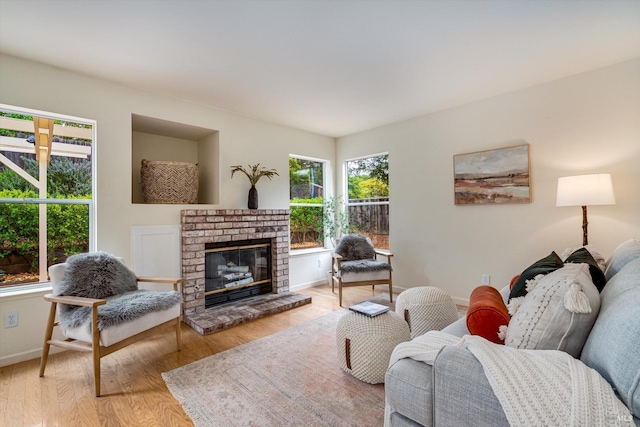 living room featuring wood finished floors, baseboards, and a brick fireplace