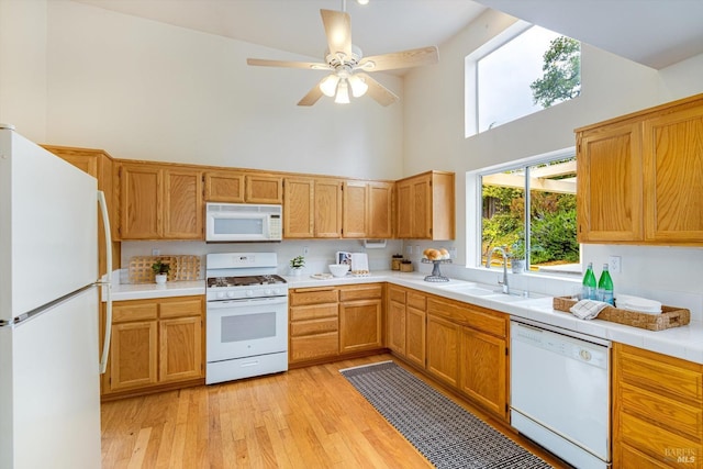 kitchen with a towering ceiling, a sink, white appliances, light wood-style flooring, and ceiling fan