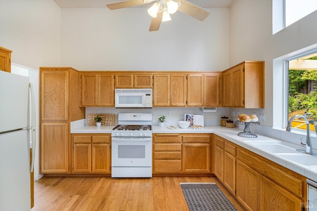 kitchen with light wood-type flooring, a towering ceiling, white appliances, and a sink